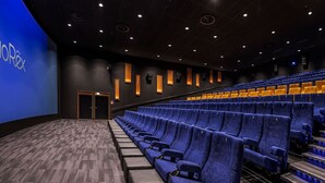 An empty movie theater with rows of blue seats, a carpeted floor, and a dark ceiling with recessed lighting.