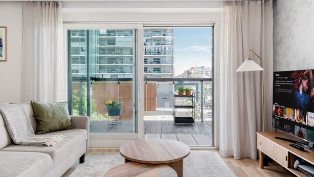 Ein modernes Wohnzimmer mit Sofa, Couchtisch, Fernseher und einem Balkon mit Topfpflanzen.