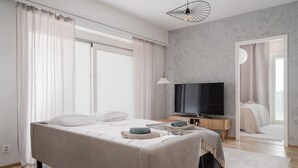 Ein modernes Schlafzimmer mit einem großen Bett, einem Fernseher und Blick auf einen anderen Raum.