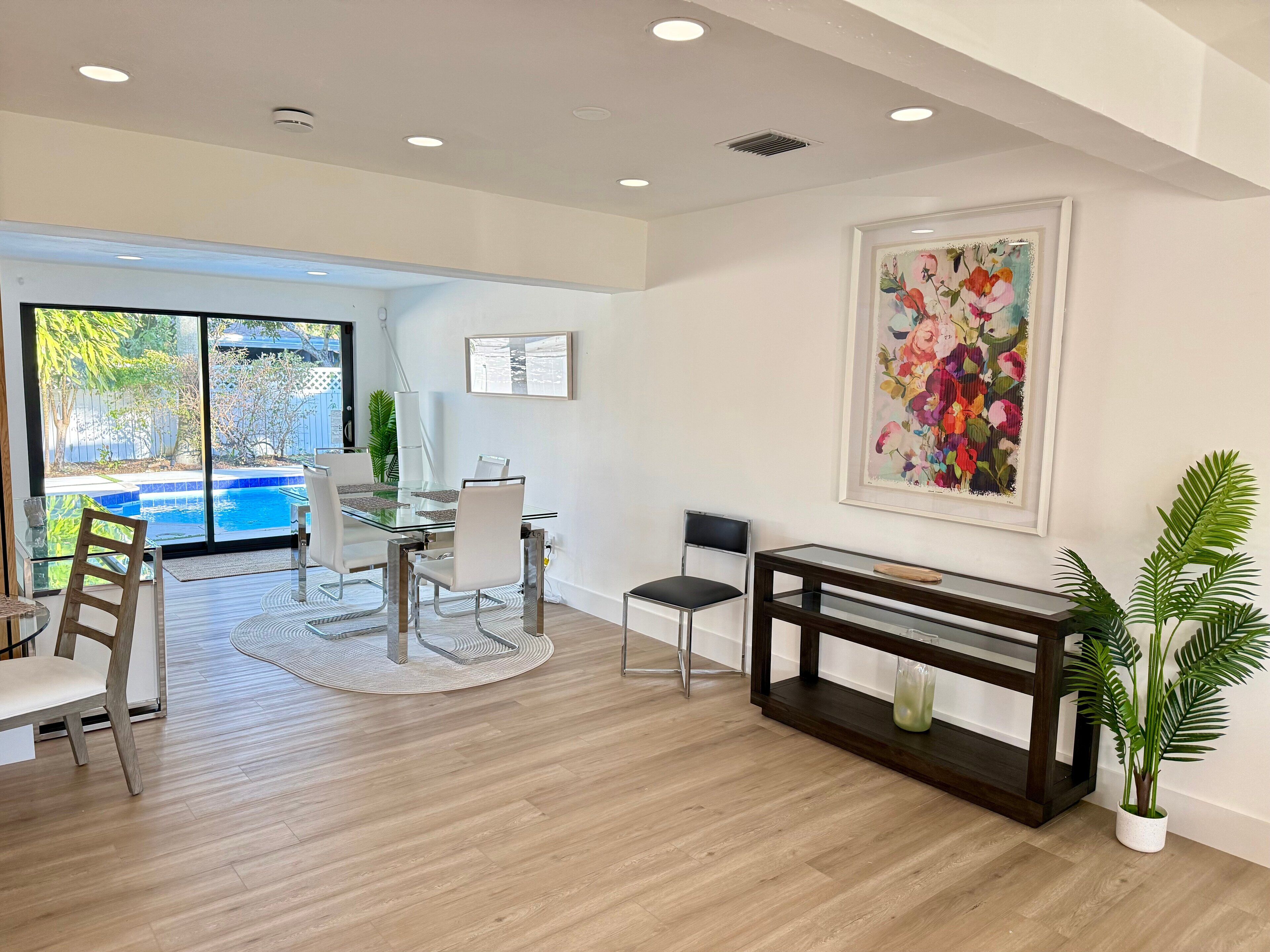 A modern dining area with a glass table, white chairs, and a wooden floor.