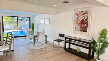 A modern dining area with a glass table, white chairs, and a wooden floor.