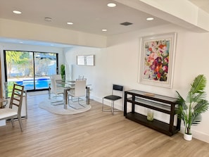 A modern dining area with a glass table, white chairs, and a wooden floor. - 3BR Oasis w/ Heated Pool, 1Gb WiFi & Near Las Olas (Fort Lauderdale)