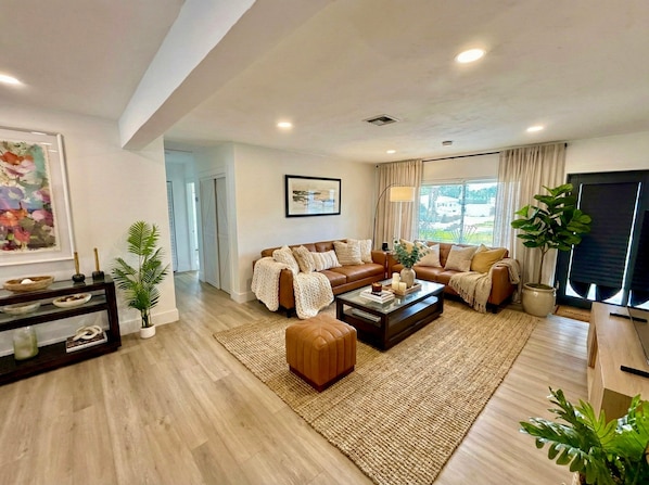 A spacious living room with a brown leather sofa set, a coffee table, and a large window with curtains. - 3BR Oasis w/ Heated Pool, 1Gb WiFi & Near Las Olas (Fort Lauderdale)