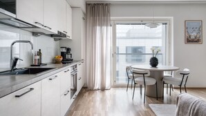 A modern kitchen with white cabinets, a stainless steel range hood, and a dining area with a round table and four chairs. - By Tripla & Train Station | King Bed · 55 TV · Gym (Helsinki)