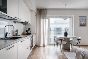 A modern kitchen with white cabinets, a stainless steel range hood, and a dining area with a round table and four chairs. - By Tripla & Train Station | King Bed · 55 TV · Gym (Helsinki)