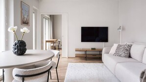 A modern living room with a round dining table, a sofa, and a flat-screen TV mounted on the wall. - By Tripla & Train Station | King Bed · 55 TV · Gym (Helsinki)