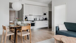 A modern kitchen with white cabinets, a dining area with wooden chairs, a blue sofa, and a white door. - Sauna, balcony, wifi, trainstation, Mall of Tripla (Helsinki)