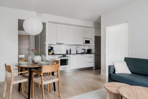 A modern kitchen with white cabinets, a dining area with wooden chairs, a blue sofa, and a white door. - Sauna, balcony, wifi, trainstation, Mall of Tripla (Helsinki)