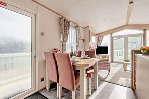 A dining area with a table set for two, a television, and a view of the outside.