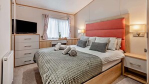 Une chambre à coucher avec un lit, une télévision, un bureau et une fenêtre avec des rideaux.