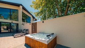 A modern outdoor hot tub area with a wooden tub, lounge chairs, and a patio table. - Cevizdibi Loft Villa (Kartepe)