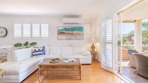 Ein modernes Wohnzimmer mit einem weißen Sofa, einem Glastisch und einem Strandbild.