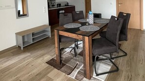 A dining area with a wooden table, grey upholstered chairs, and a bench. A kitchen is visible in the background. - Spacious vacation apartment on the edge of Saxon Switzerland (Stolpen)