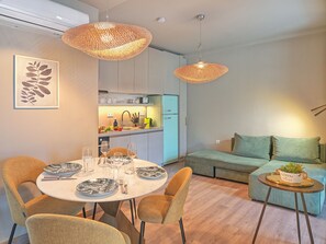 Una sala de estar moderna con comedor, que presenta una mesa redonda preparada para cuatro personas, un sofá y una mesita auxiliar con una planta.
