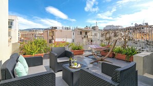 A rooftop terrace with wicker furniture, potted plants, and a glass table with a bottle and glasses. - Karitsi Suites (Athens)