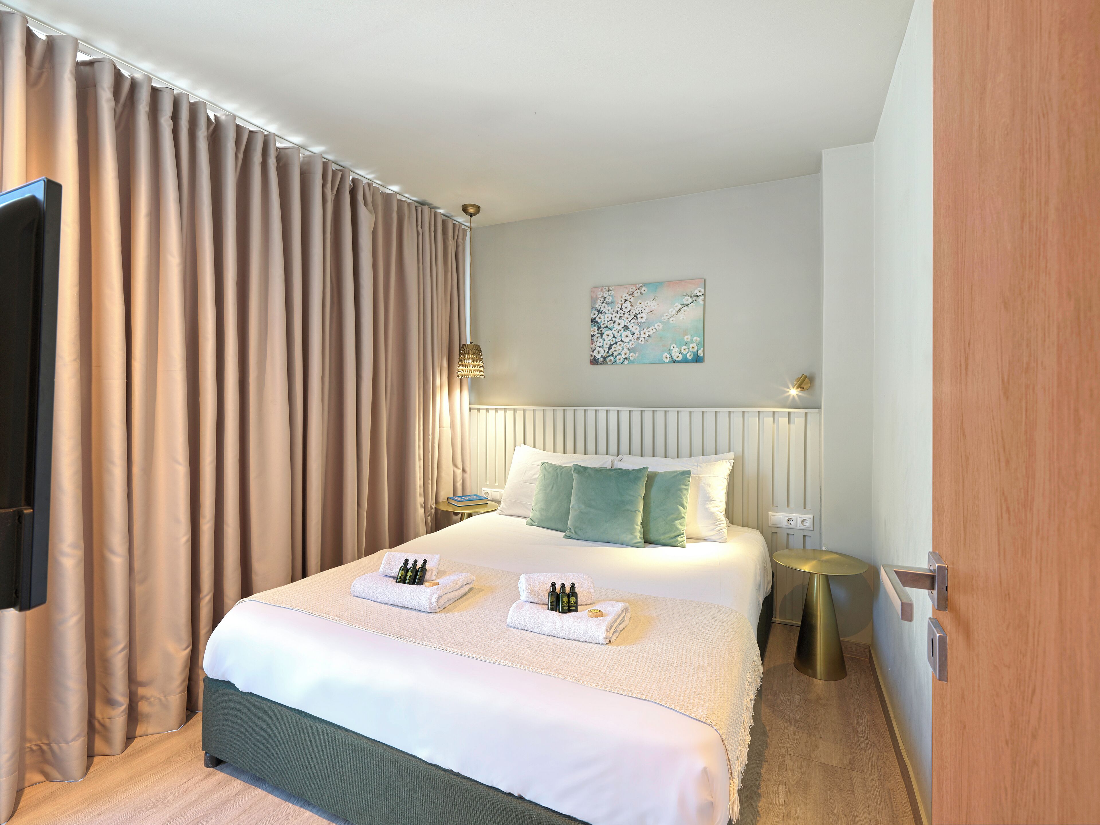 Een opgemaakt bed met kussens, een nachtkastje met een lamp, en een schilderij aan de muur.