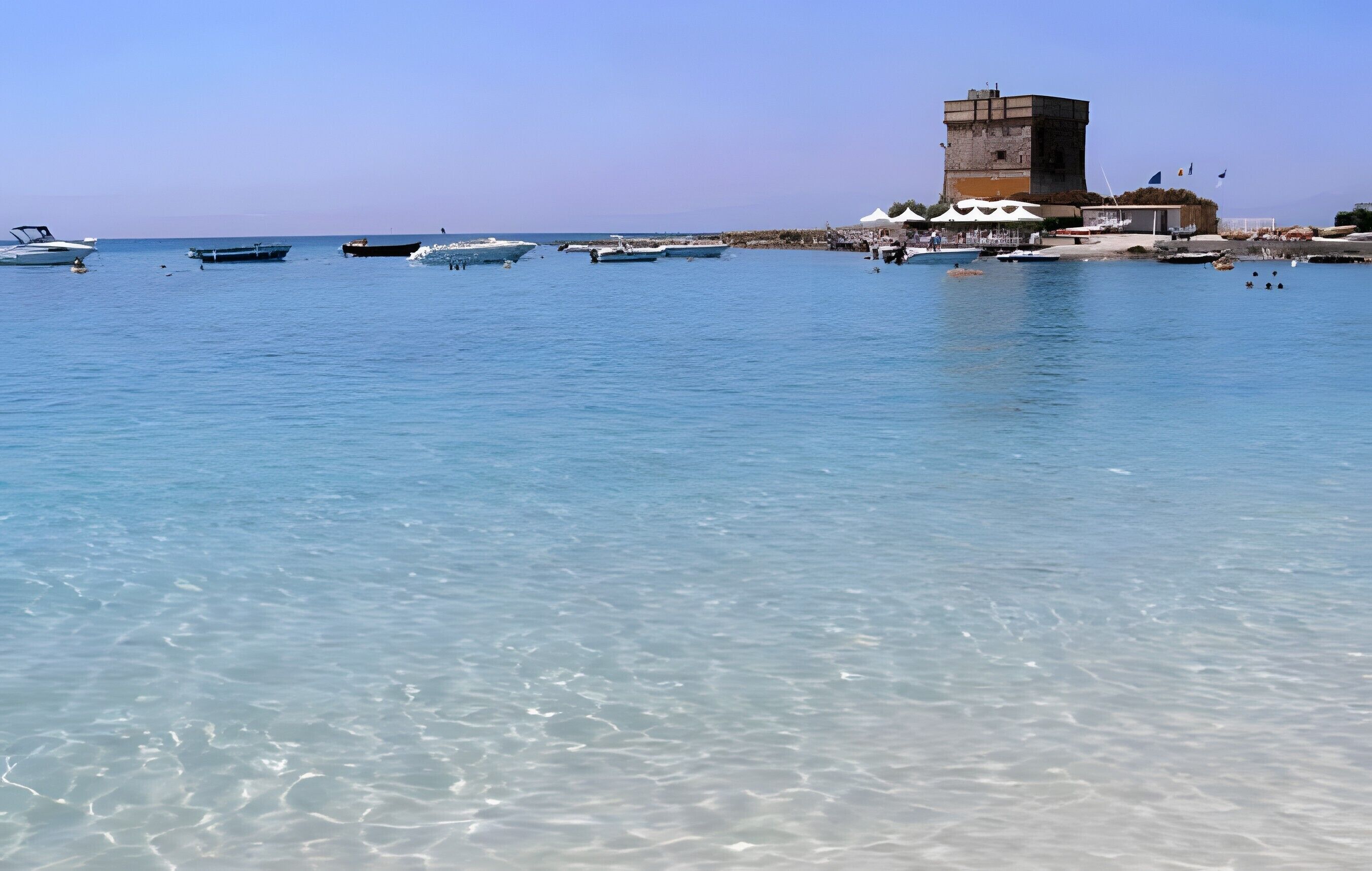 Zona costera con barcos amarrados, una torre y tiendas de campaña instaladas para un evento.