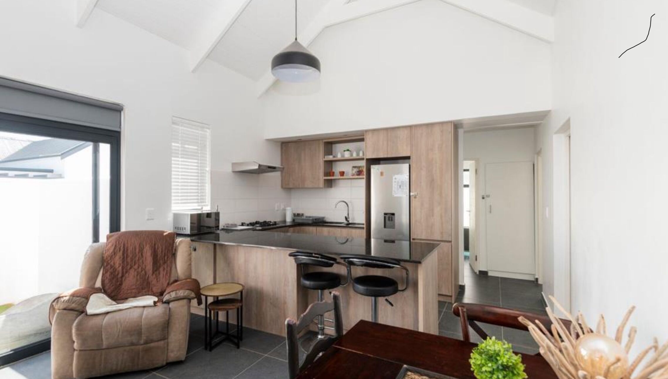 A modern kitchen with a central island, wooden cabinets, and a stainless steel refrigerator.