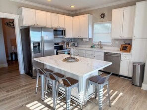 Una cocina moderna con armarios blancos, electrodomésticos de acero inoxidable y una isla central con taburetes de bar.