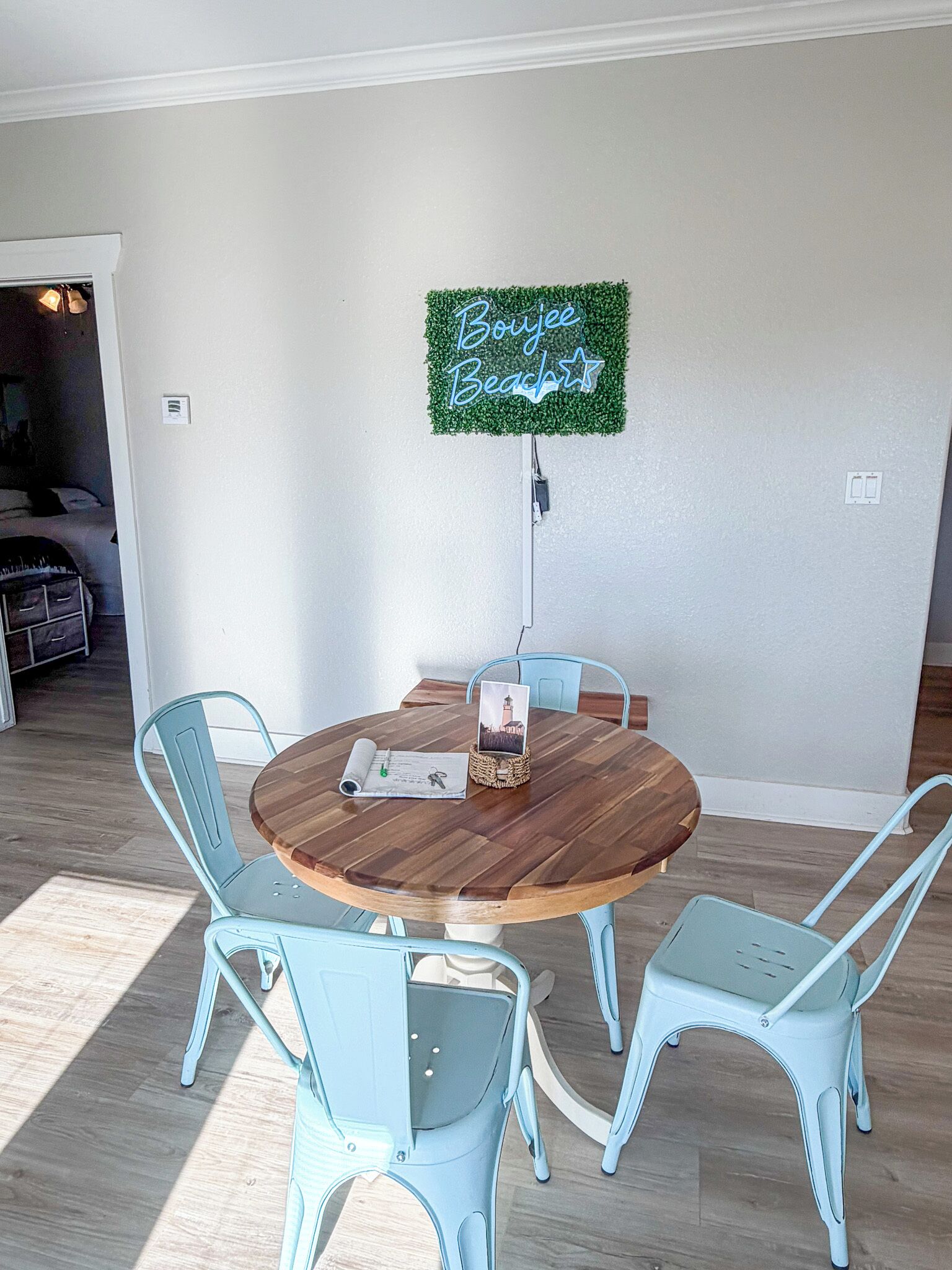 A dining area with a round wooden table, four light blue chairs, and a neon sign on the wall.