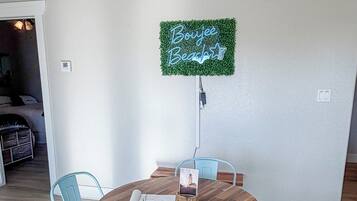 A dining area with a round wooden table, four light blue chairs, and a neon sign on the wall.