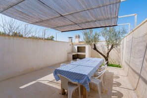 Een terras buiten met een tafel, stoelen, een barbecue en een beschaduwd gedeelte.