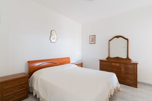 Een slaapkamer met een bed, een houten dressoir en een spiegel.