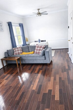 Un salon avec un canapé gris, une table basse en bois et un ventilateur de plafond.