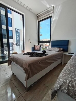 Ein Schlafzimmer mit einem Bett, einem Nachttisch, einem Sessel, einem Fenster und einem Balkon.