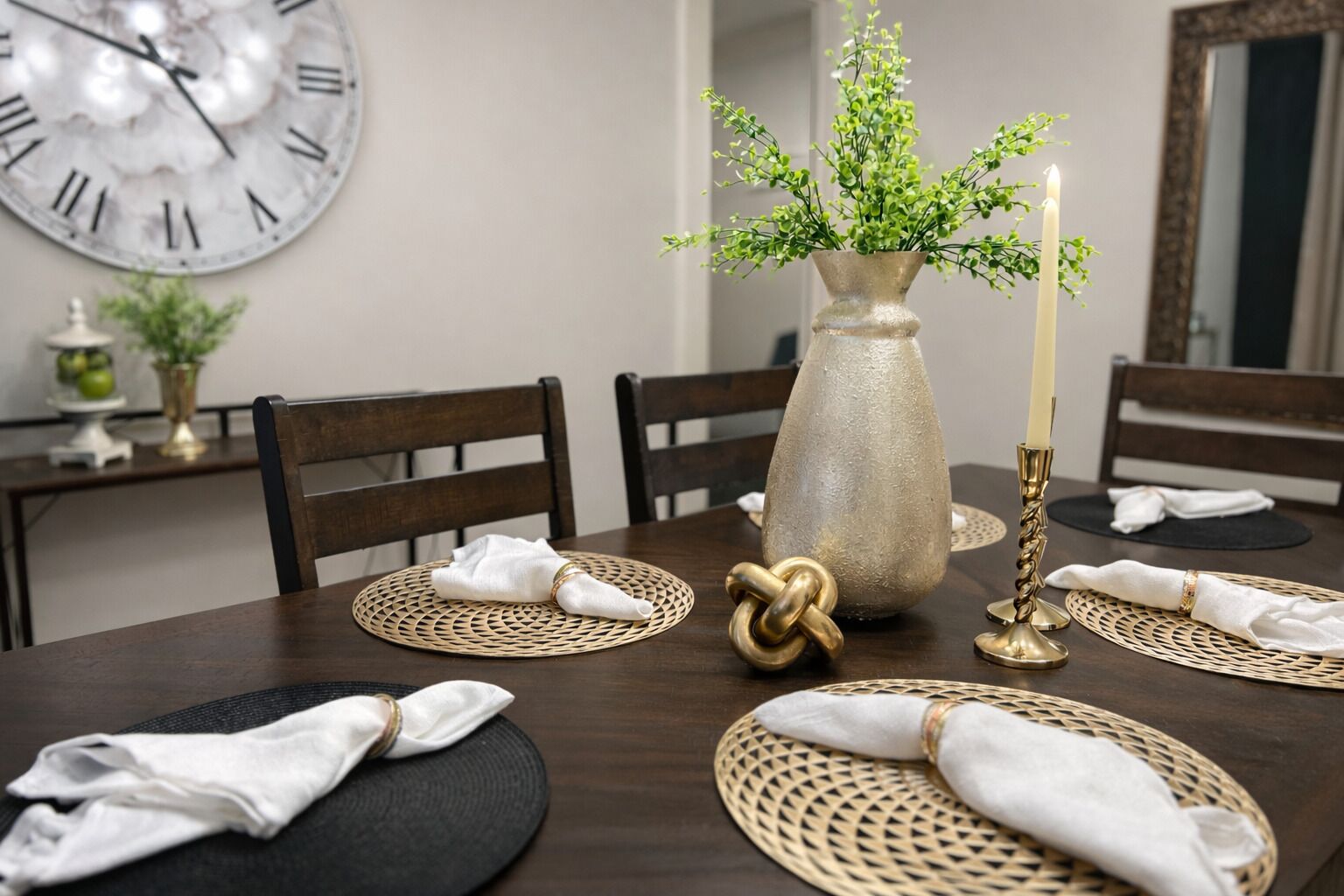 A dining table set with placemats, a vase with greenery, and a candle holder.