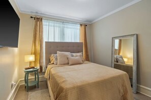 A neatly arranged bedroom with a large bed, a bedside table with a lamp, and a mirror on the wall.