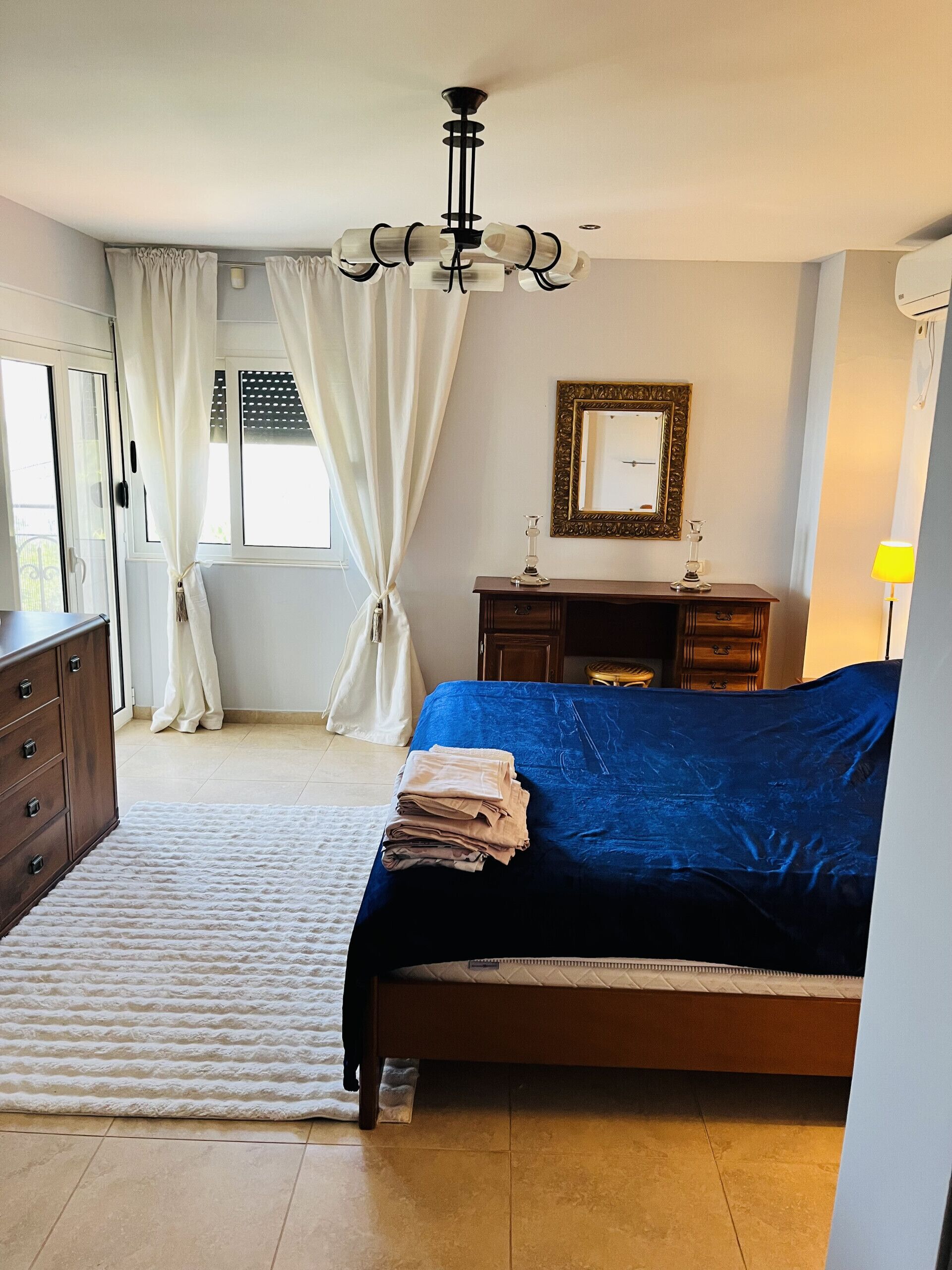 A bedroom with a bed, a dresser, a mirror, and a chandelier.
