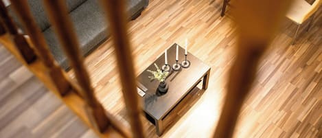 Un salon moderne avec un plancher en bois, un canapé gris et une table basse agrémentée de bougies et d’un vase.