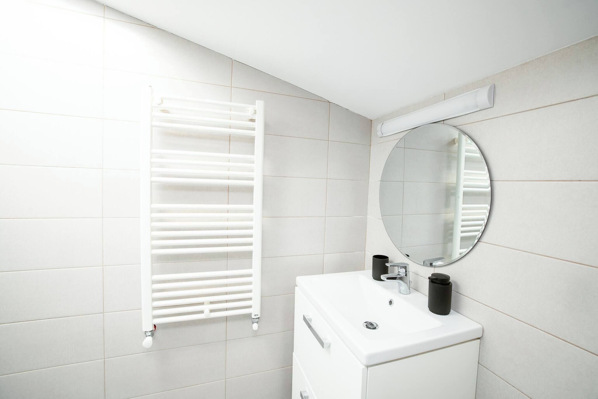 Un bany amb un lavabo blanc, un mirall rodó i un penjador de tovalloles blanc.