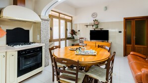 Una cocina con estufa, horno, mesa de comedor con sillas, televisor y sofá.