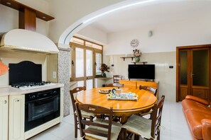 Eine Küche mit Herd, Backofen, Esstisch mit Stühlen, einem Fernseher und einer Couch.