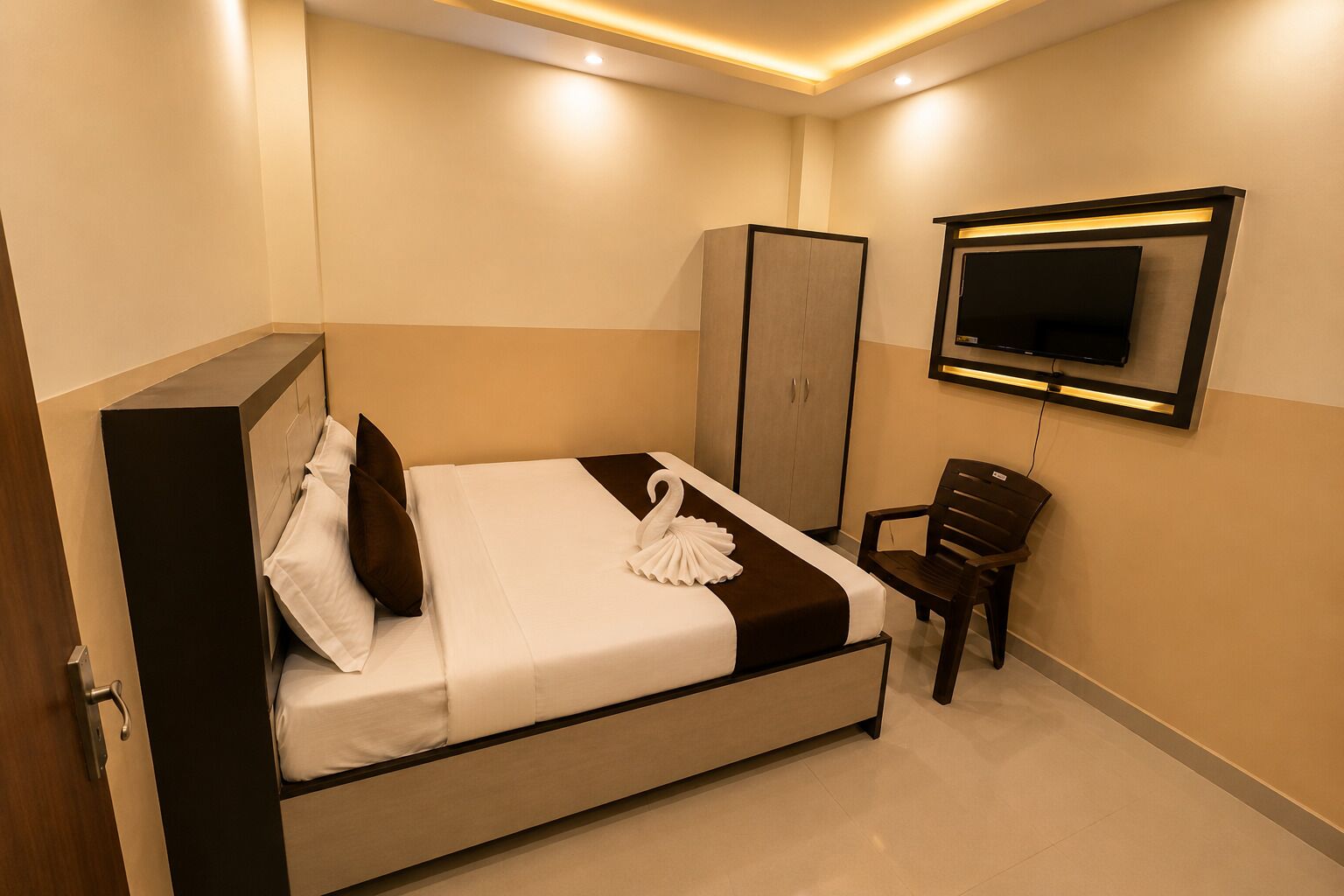 A hotel room with a bed, a wardrobe, a chair, and a flat-screen TV mounted on the wall.