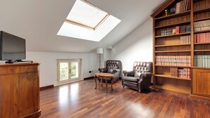 Una habitación amplia con tragaluces, una estantería grande, un sillón de cuero y un aparador de madera.