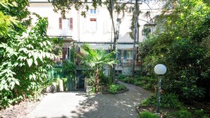 Un patio con un sendero adoquinado, vegetación, un objeto esférico blanco y un edificio con balcones.