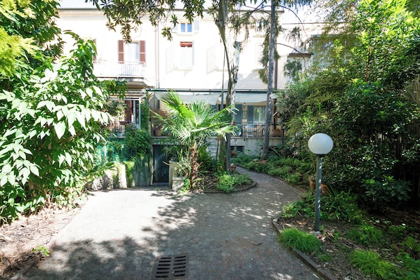 A courtyard with a cobblestone path, greenery, a white spherical object, and a building with balconies.