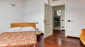 Un dormitorio con cama de madera, colcha estampada, puerta blanca que da al baño y suelo de madera.