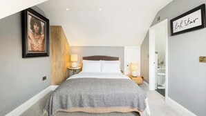A bedroom with a bed, bedside lamps, a framed picture on the wall, and a door leading to a bathroom. - Well Located, Cheltenham 4 Bed Townhouse & Parking (Gloucestershire)