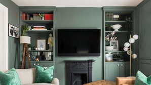 A living room with a sofa, armchair, and ottoman, a fireplace, a television, and built-in shelving with books and decorative items. - Well Located, Cheltenham 4 Bed Townhouse & Parking (Gloucestershire)