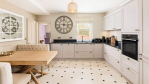 A modern kitchen with white cabinets, a wooden dining table, and a black and white patterned floor. - Well Located, Cheltenham 4 Bed Townhouse & Parking (Gloucestershire)