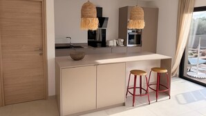 Una cocina moderna con una isla central, dos lámparas colgantes de mimbre y un horno empotrado, además de un amplio ventanal con vistas.
