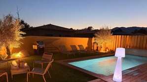 Un patio trasero con piscina, sillas de descanso, una parrilla y un farol.