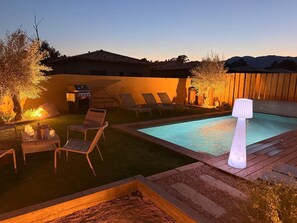 Ein Garten mit Schwimmbad, Liegestühlen, Grill und einer Laterne.