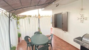 A patio with a table and chairs, a grill, and a TV mounted on the wall. - Holiday Home 'Dall'alba Al Tramonto' with Private Terrace, Wi-Fi and Air Conditioning (Alezio)
