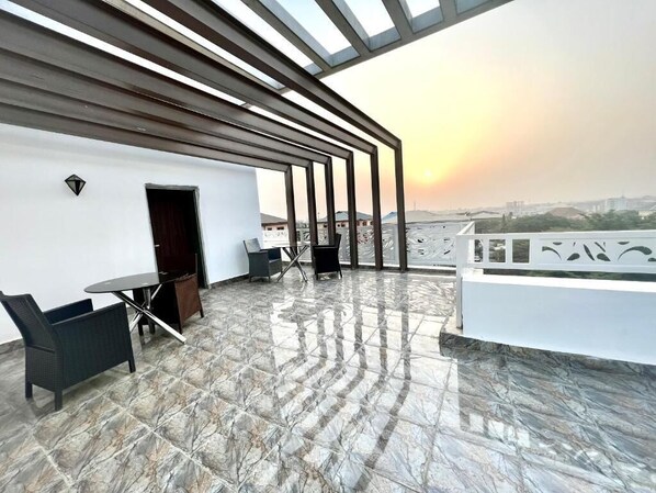 Una terraza en la azotea con vistas al horizonte de la ciudad al atardecer, con un diseño moderno que incluye una pérgola, un área de estar y una puerta.