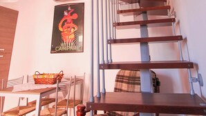 A staircase with a wooden handrail and metal balusters, a dining area with chairs and a table, and a wall-mounted air conditioning unit. - Casa Vacanze La Fonda (Santo Stefano di Magra)